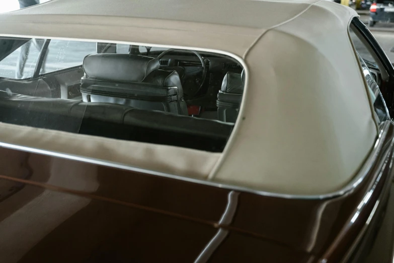 a brown and white car parked in a garage, a hyperrealistic painting, unsplash, photorealism, 1 9 7 0 s car window closeup, soft top roof raised, view from behind mirror, replica model