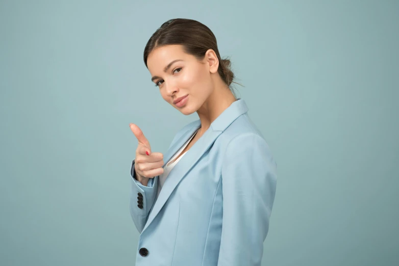 a woman in a blue suit giving a thumbs up, by Julia Pishtar, trending on pexels, figuration libre, gal gadot, pastel', brunette woman, with index finger