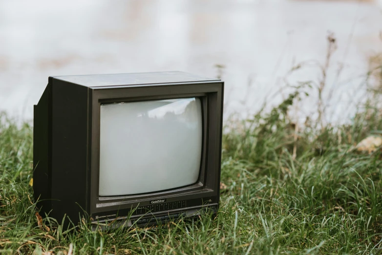 an old television sitting in the grass next to a body of water, unsplash, video art, instagram post, 1 9 8 0 s photo, programming, cast