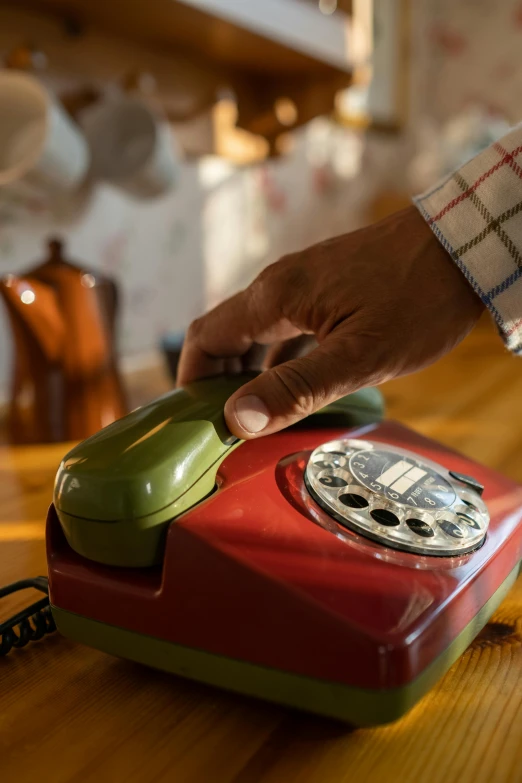 a red and green telephone sitting on top of a wooden table, hands on counter, vintage vibe, playing, brown