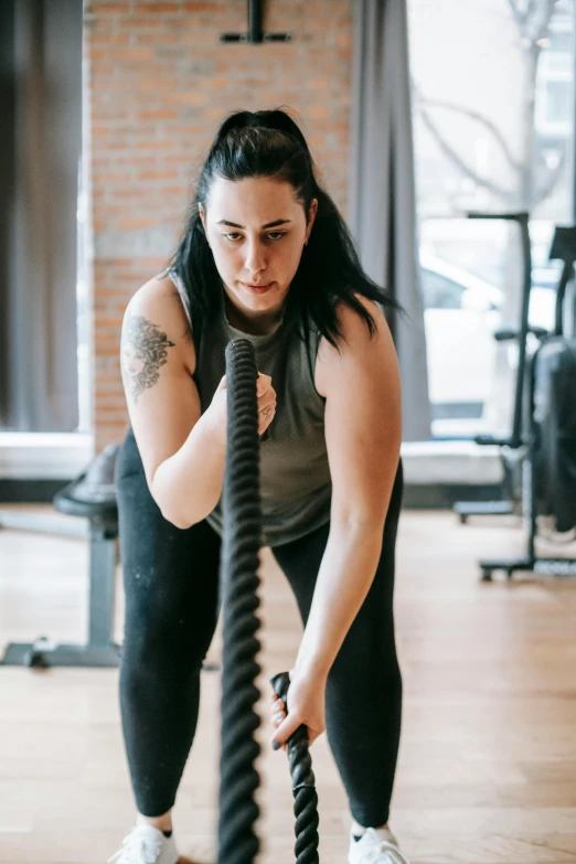 a woman holding a rope in a gym, by Arabella Rankin, she is wearing a black tank top, kyle hotz, profile image