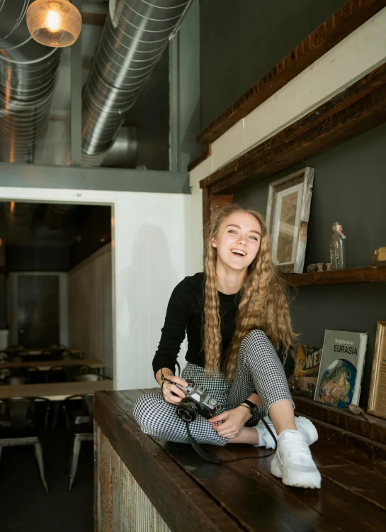 a woman sitting on top of a wooden counter, by Julia Pishtar, pexels contest winner, smiling girl, pale skin curly blond hair, small hipster coffee shop, dslr photo of a pretty teen girl