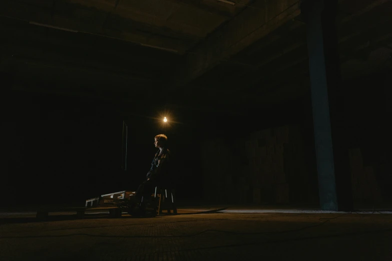 a man standing next to a bench in a dark room, performing a music video, set inside of parking garage, jovana rikalo, kneeling