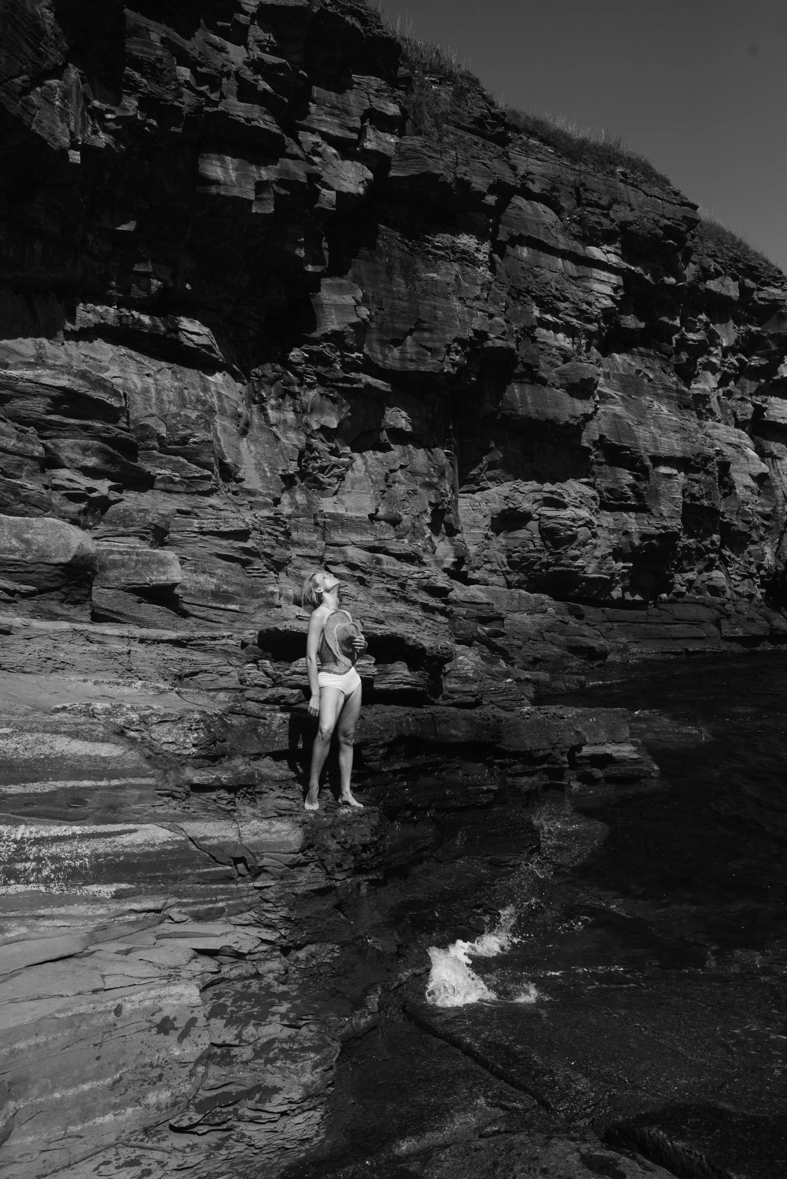 a woman sitting on a rock next to a body of water, inspired by Max Dupain, syd meade, circa 1958, [ cinematic, mid-shot of a hunky