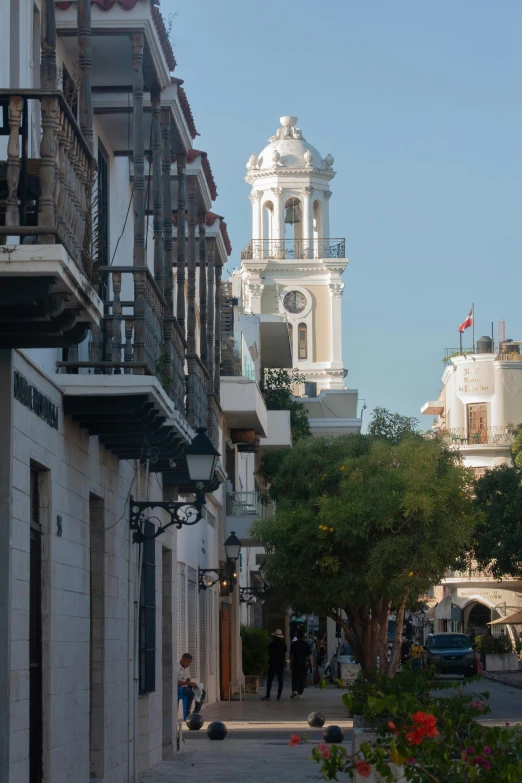 a clock tower towering over a city street, inspired by Joaquín Torres García, renaissance, neoclassical tower with dome, puerto rico, terraces, narrow street