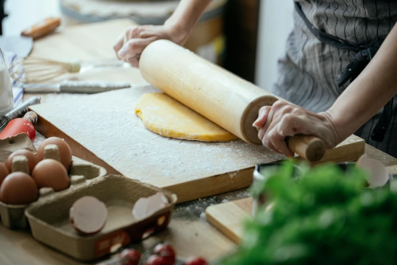 a woman rolling out dough on a cutting board, a picture, by Jessie Algie, trending on pexels, scrolls, seasonal, pastry, battered