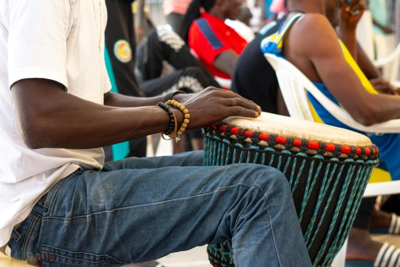 a man that is sitting down with a drum, pexels contest winner, black arts movement, unmistakably kenyan, tournament, center of image, closeup of arms