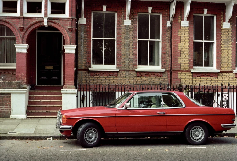 a red car parked in front of a brick building, inspired by Thomas Struth, 7 0 s street photography, mercedez benz, in style of alasdair mclellan, 2 0 0 4 photograph