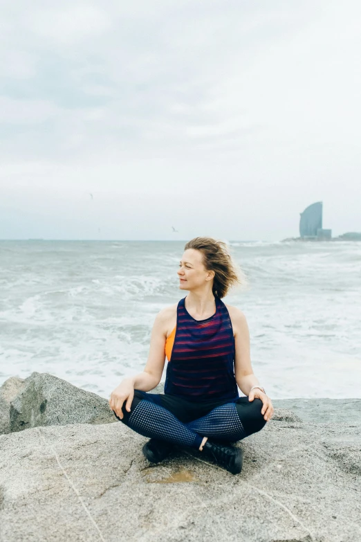 a woman sitting on top of a rock next to the ocean, in barcelona, sitting cross-legged, icon, beth cavener