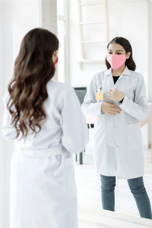 a woman in a lab coat standing in front of a mirror, a picture, shutterstock, happening, masked doctors, cardboard cutout, pink, talking