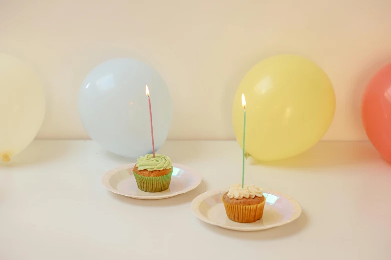 a cupcake sitting on top of a plate next to balloons, natural candle lighting, single flat colour, evenly lit, pastel'