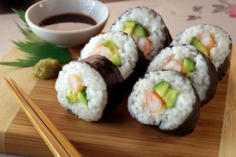 a wooden cutting board topped with sushi and chopsticks, a picture, prawn, avocado, yoko d'holbachie, rice