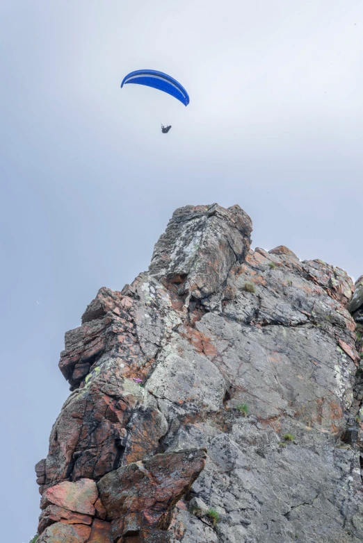 a paraglider flying over a rocky outcropping, hestiasula head, hanging upside down, photo taken in 2018, minn