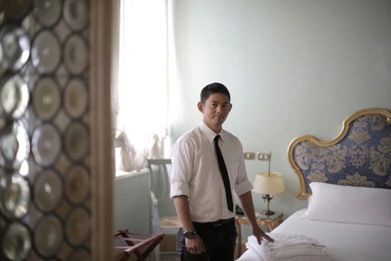 a man standing in a bedroom next to a bed, a portrait, inspired by Ding Yunpeng, unsplash, formal attire, young handsome pale roma, tourist photo, working