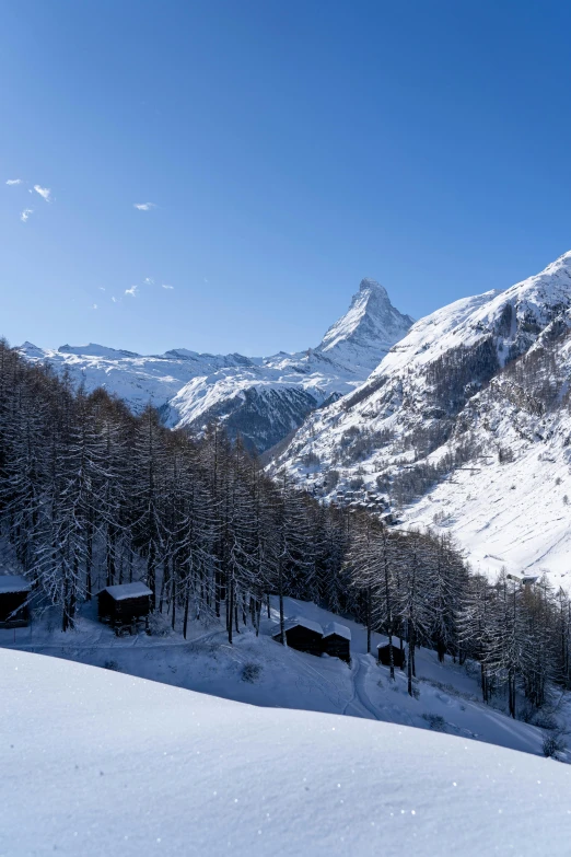 a group of people riding skis down a snow covered slope, log cabin beneath the alps, overlooking a valley with trees, rivendell, clear blue skies