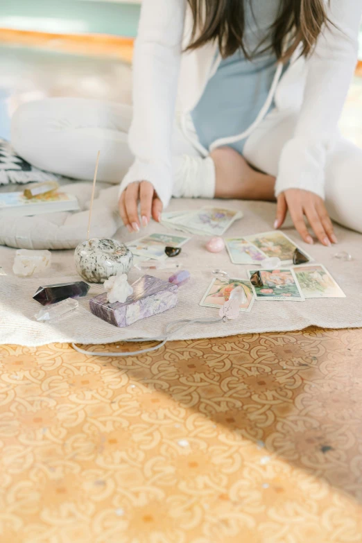 a woman sitting on the floor drawing on a piece of paper, a polaroid photo, by Julia Pishtar, trending on pexels, iridescent crystals, tarot design, in a silver silk robe, pastel'