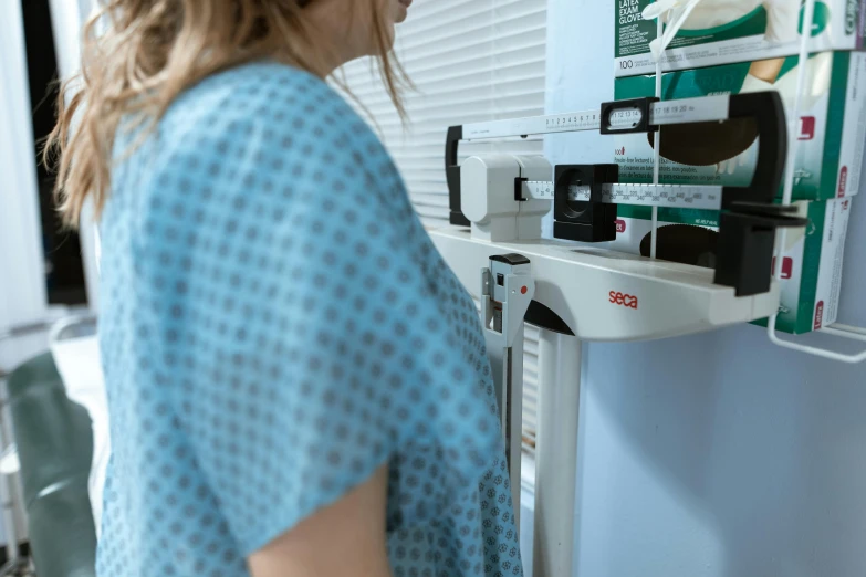 a woman standing in front of a machine, pexels, nurse scrubs, profile image, scales covering her chest, colour photograph