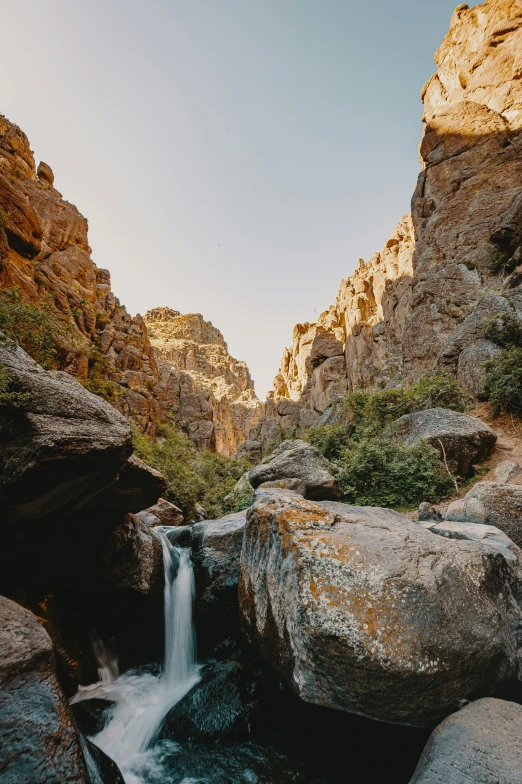 a small waterfall in the middle of a canyon, by Kristin Nelson, ultrawide image, tall big rocks, long