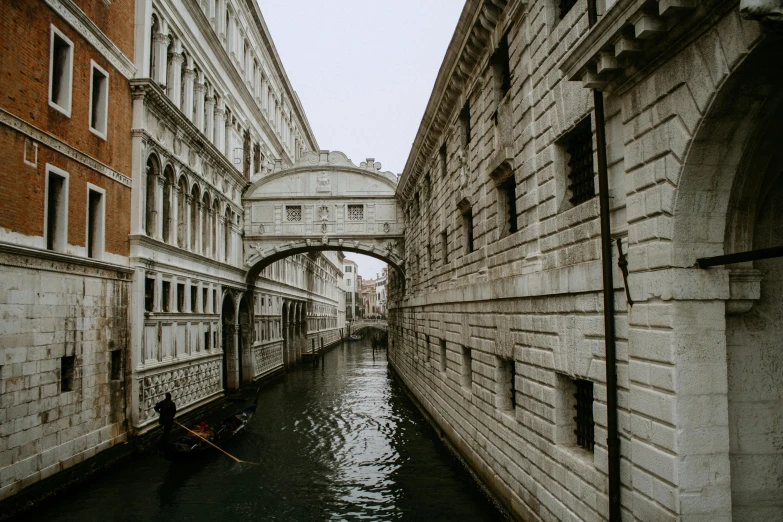 a narrow canal with a gondola going under a bridge, inspired by Michelangelo Buonarotti, pexels contest winner, renaissance, grey, body of water, grain”, 1940s photo