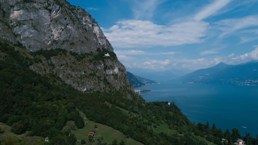 a large body of water sitting on top of a lush green hillside, by Daniel Lieske, pexels contest winner, renaissance, the alps are in the background, aerial footage, cliff side, youtube thumbnail