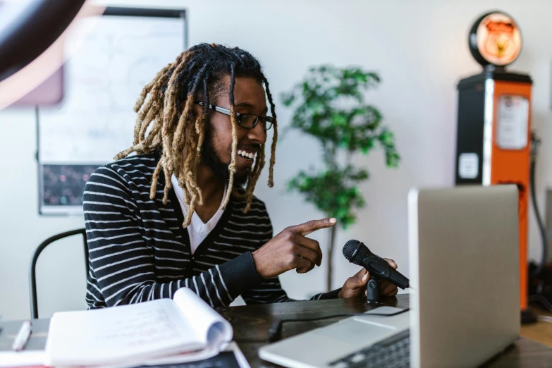 a man with dreadlocks sitting in front of a laptop, by Everett Warner, pexels contest winner, holding microphone, teaching, lachlan bailey, high quality screenshot