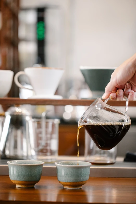 a person pours coffee into two cups, by Jessie Algie, glassware, over-shoulder shot, straining, premium quality