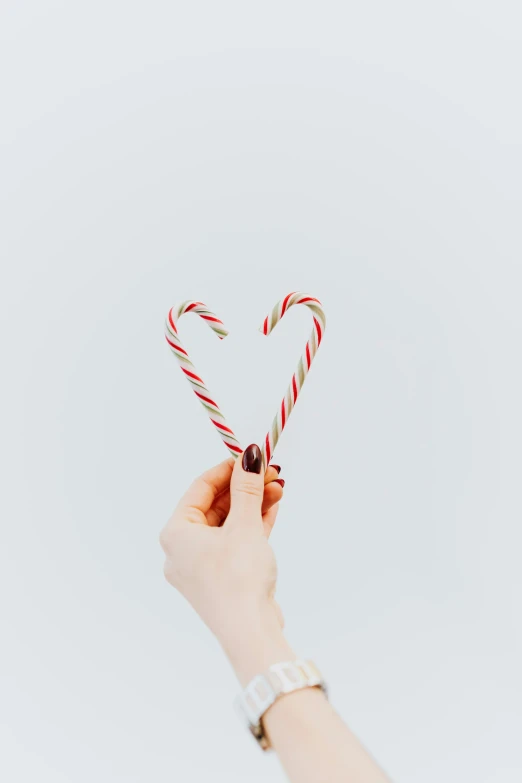 a person holding a candy cane in the shape of a heart, pexels, minimalism, 🐿🍸🍋, multiple stories, canva, festive