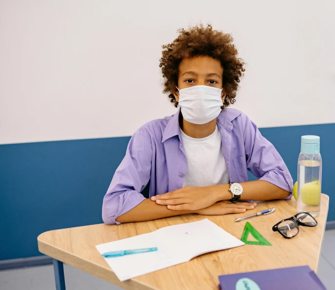 a woman sitting at a table wearing a face mask, trending on pexels, paris school, black teenage boy, surgeon, aida muluneh, no duplicate image