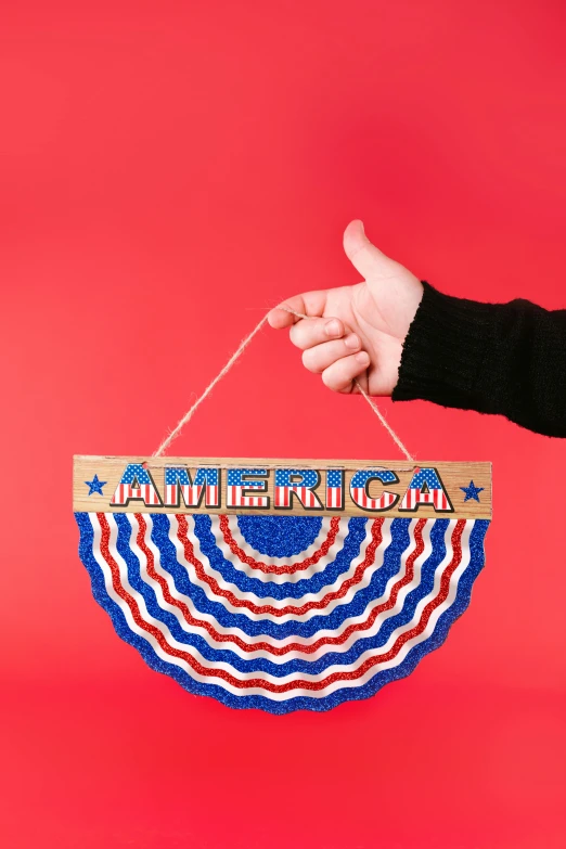 a person holding an american flag hanging from a string, inspired by Americo Makk, kinetic art, fully decorated, sign, full product shot, rebecca sugar