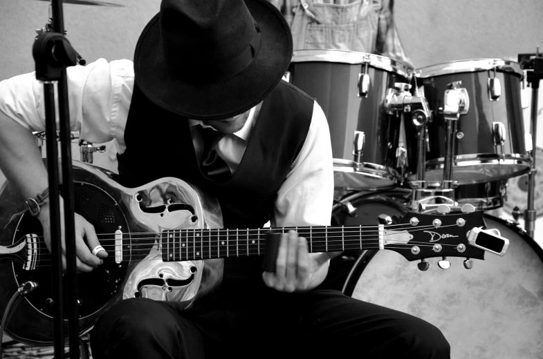 a black and white photo of a man playing a guitar, a black and white photo, by Mike Bierek, a suited man in a hat, holding electric guitars, outside on the ground, closeup!!!!!