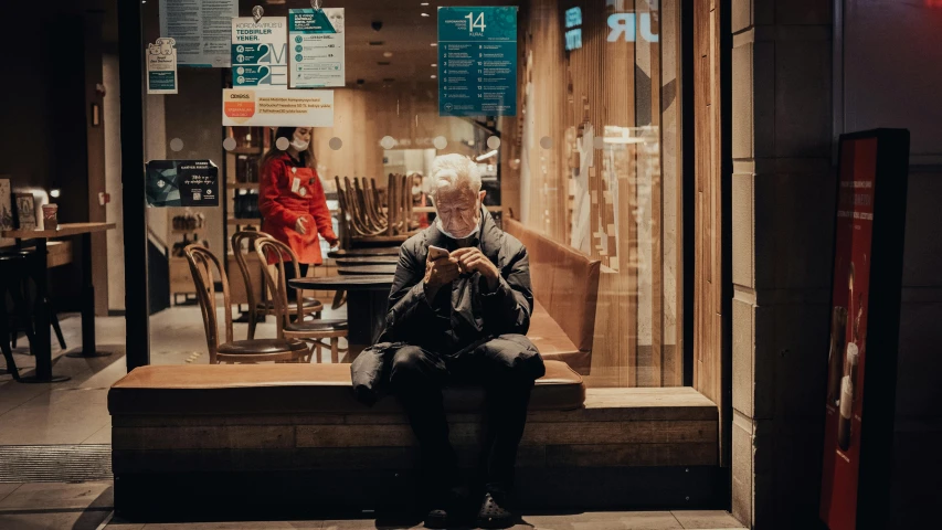 a person sitting on a bench in front of a store, pexels contest winner, cyberpunk old man, cellphone, ad image