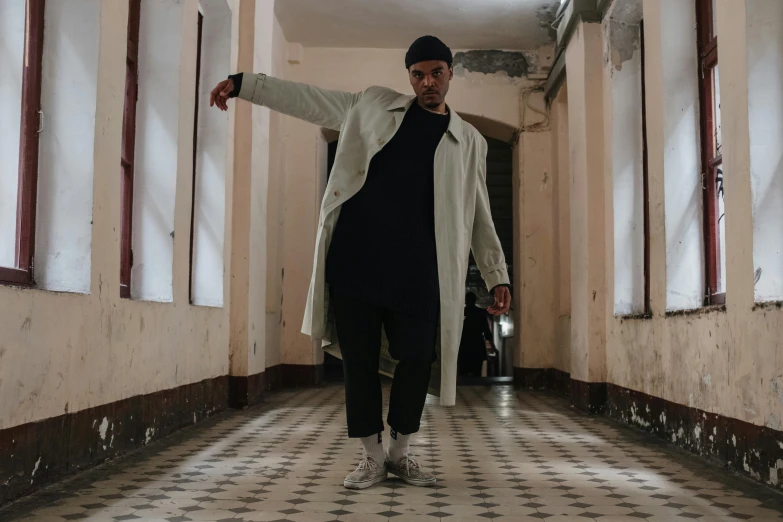 a man in a long coat standing in a hallway, an album cover, pexels contest winner, antipodeans, classic dancer striking a pose, ( ( theatrical ) ), berghain, wearing off - white style