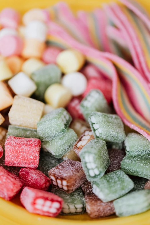 a yellow bowl filled with assorted candies, a colorized photo, inspired by Judy Takács, trending on pexels, green and pink fabric, muted rainbow tubing, close up of single sugar crystal, squares