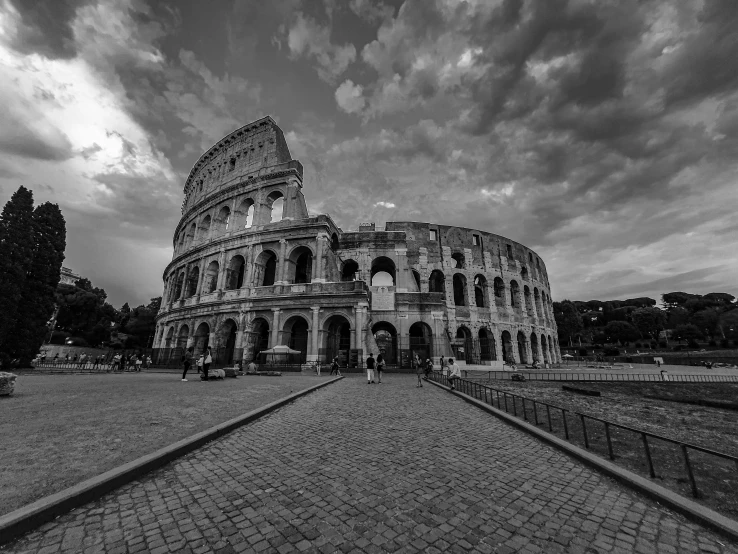 a black and white photo of the colossion, by Daniel Gelon, pexels contest winner, neoclassicism, colosseum, ground view, summer evening, clouds around