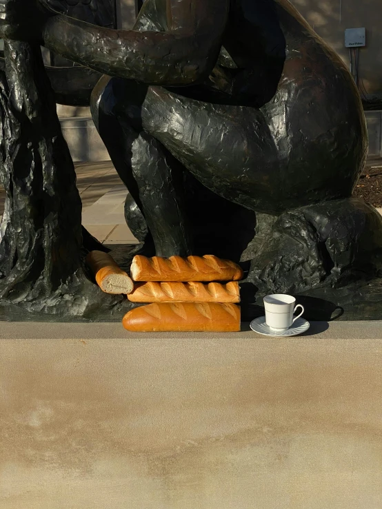 a statue of a man with bread and a cup of coffee, inspired by Aristide Maillol, realism, joel meyerowitz, [sculpture] and [hyperrealism], baking french baguette, set photograph