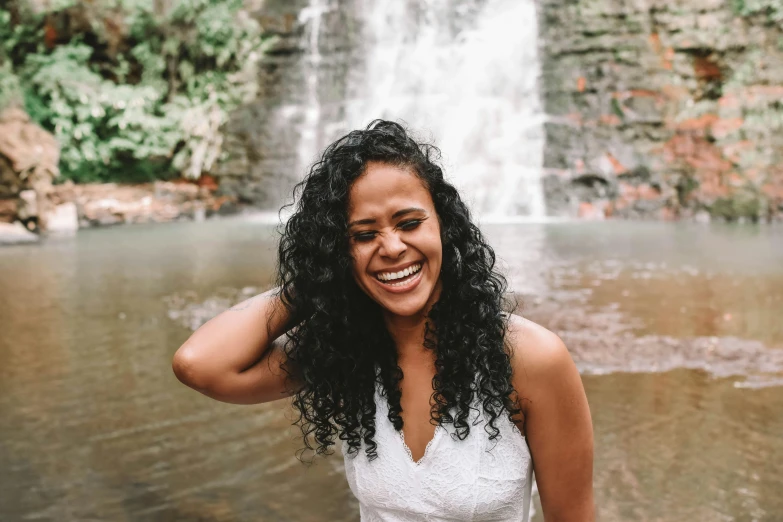 a woman standing in front of a waterfall, by Jessie Algie, pexels contest winner, hurufiyya, dark short curly hair smiling, brazilian, her hair is white, sydney park