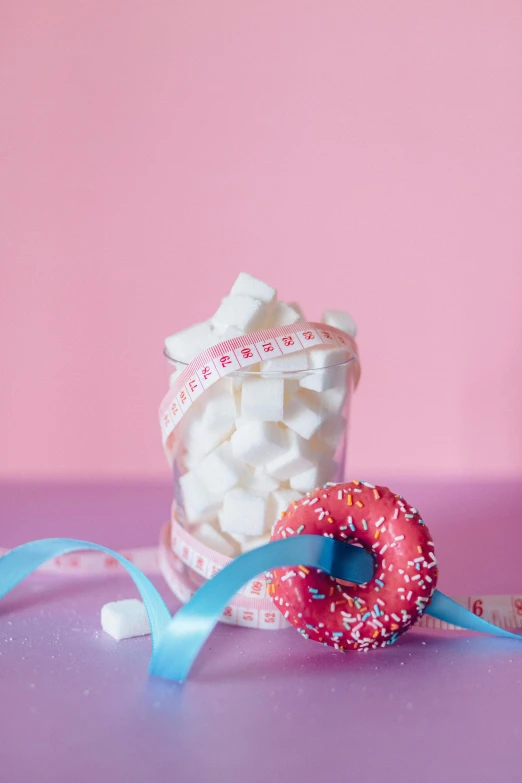 a donut sitting on top of a table next to a jar of marshmallows, by Elsa Bleda, pexels contest winner, ribbon, fitness, white and pink, made out of sweets