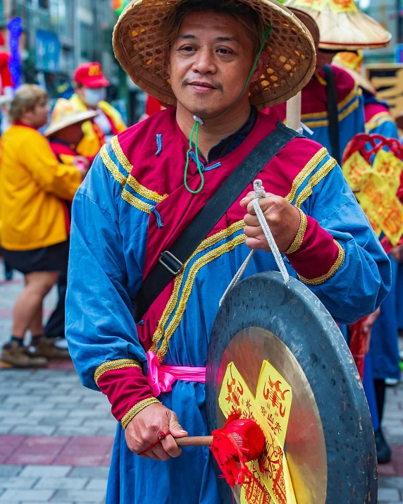 a man that is standing in the street with a drum, inspired by Gong Xian, pexels contest winner, cloisonnism, red and teal and yellow, 2 0 2 2 photo, wearing a round helmet, square