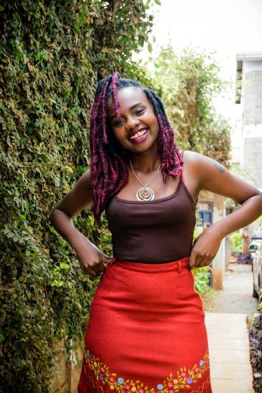 a woman in a red skirt posing for a picture, by Ella Guru, pexels contest winner, afrofuturism, smiling young woman, lush surroundings, she is about 1 6 years old, physical : tinyest midriff ever