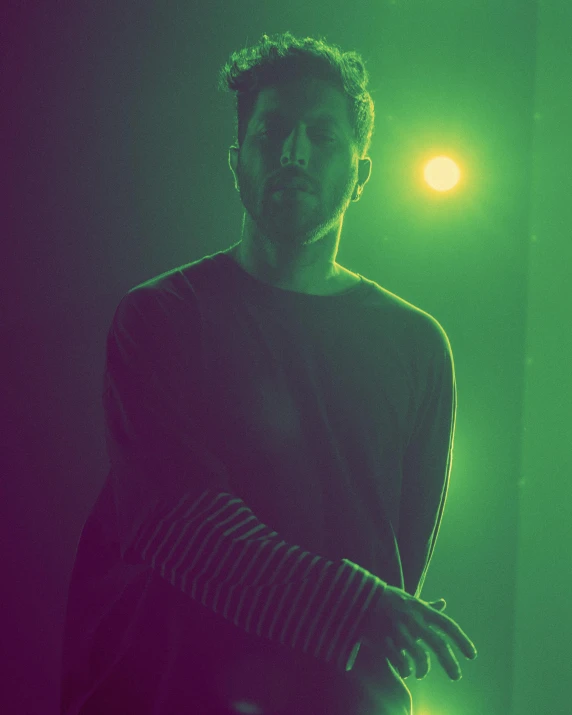 a man standing in front of a green light, inspired by Elsa Bleda, mannerism, rainbow overlay! beautifully lit, mid-shot of a hunky, mark edward fischbach, desaturated