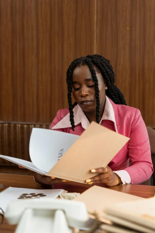 a woman sitting at a table reading a book, an album cover, by Barthélemy Menn, pexels contest winner, in a courtroom, young thug, wearing a light - pink suit, documents