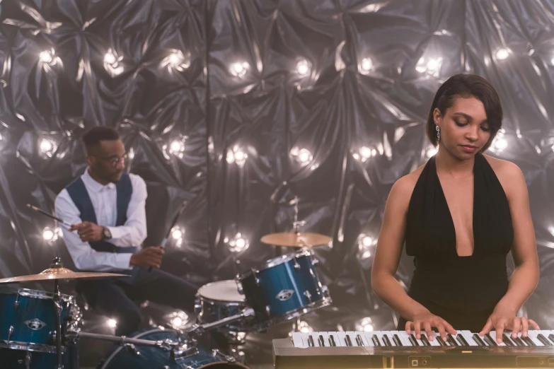 a woman in a black dress playing a keyboard, an album cover, pexels, happening, still frame from a movie, moonlight, playing drums, jordan lamarre - wan