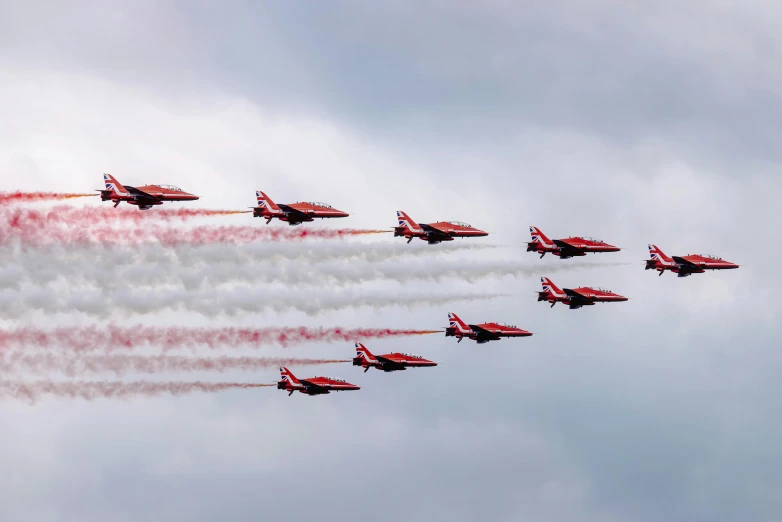 a group of fighter jets flying through a cloudy sky, by Paul Bird, pexels contest winner, wearing red attire, wales, 🦩🪐🐞👩🏻🦳, curved red arrow