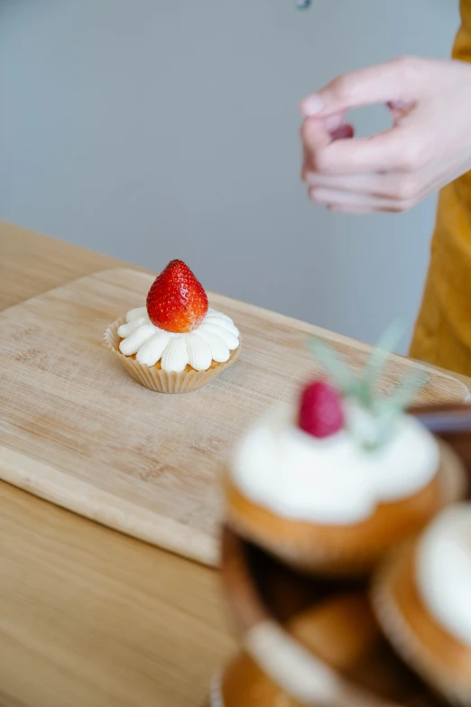 a person standing in front of a cutting board with cupcakes on it, a still life, by Andries Stock, trending on pexels, strawberry, white, on a wooden tray, smooth details