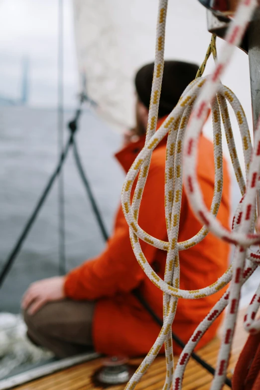 a couple of people sitting on top of a boat, belaying, zoomed in, warm coloured, sailor clothing