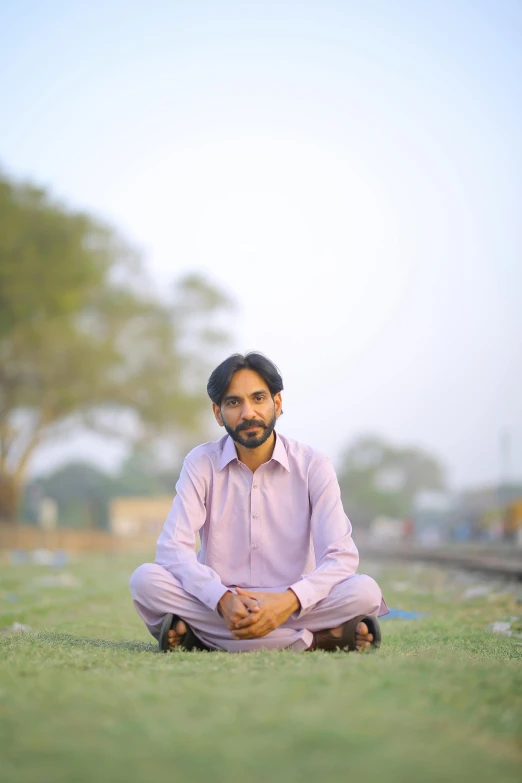 a man sitting on top of a lush green field, by Riza Abbasi, in the background, train far, profile picture, standing in road