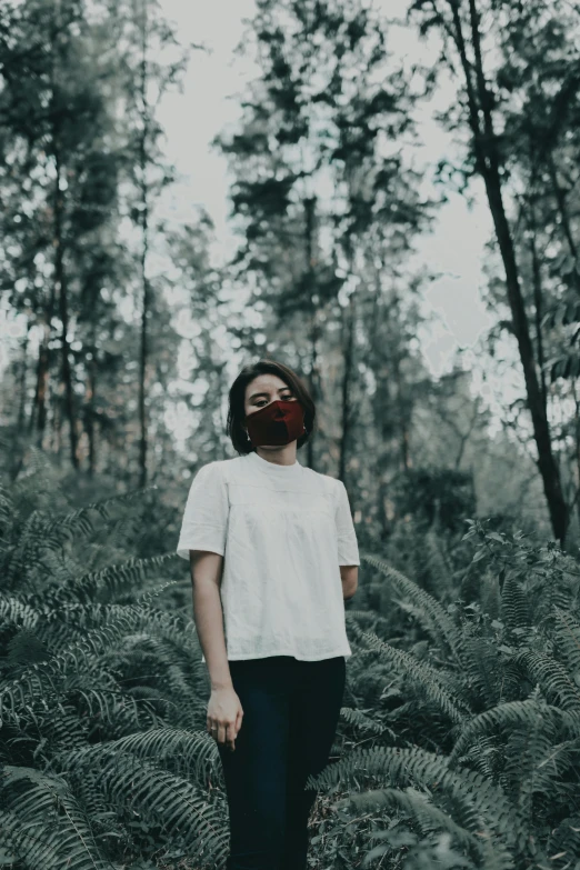 a woman standing in the middle of a forest, one single mask, dressed in a white t shirt, slightly red, unsplash photography