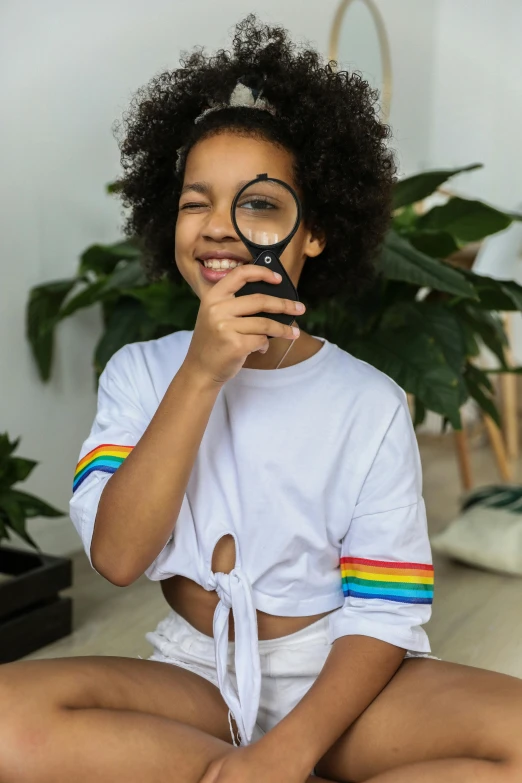 a woman sitting on the floor looking through a magnifying glass, by Julia Pishtar, pexels contest winner, super cute funky black girl, rainbow clothes, girl standing, closeup of an adorable