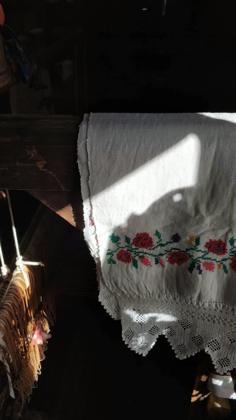 a white table cloth sitting on top of a wooden table, folk art, shaft of sun through window, embroidery, barn, shawl