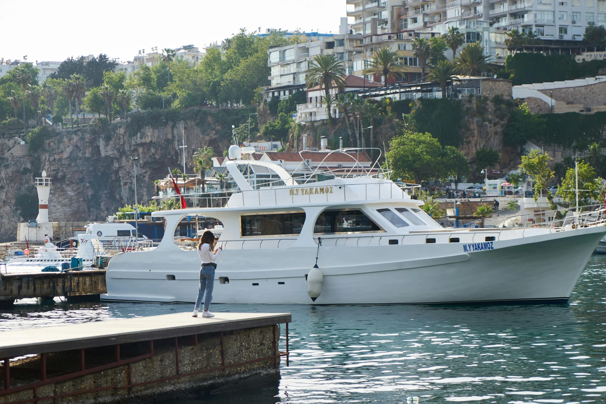 a man standing on a dock next to a boat, simona sbaffi is the captain, cliffs, shaped like a yacht, around the city